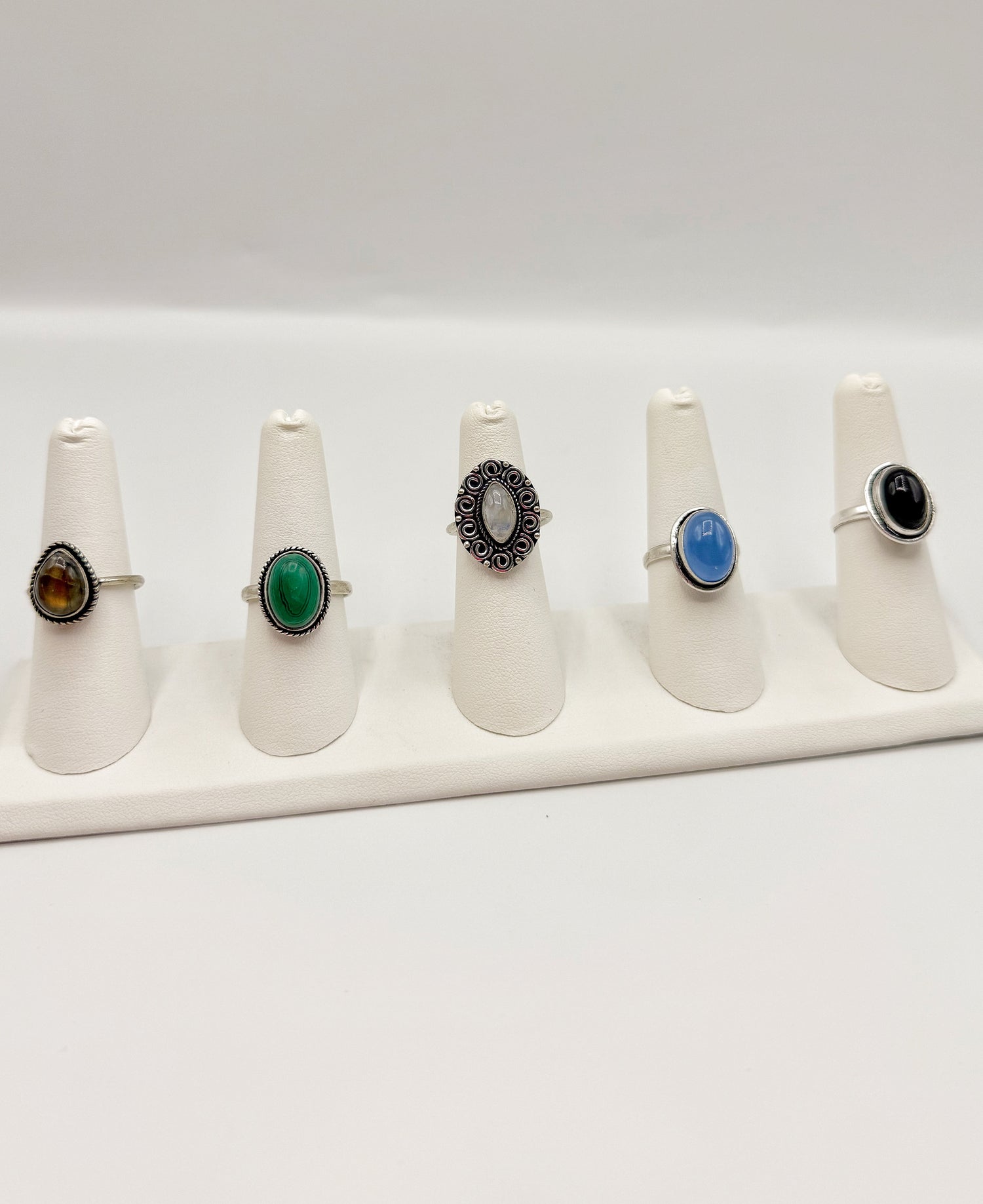 Gemstone ring set on display stands with blue, green, and black stones, silver-tone
