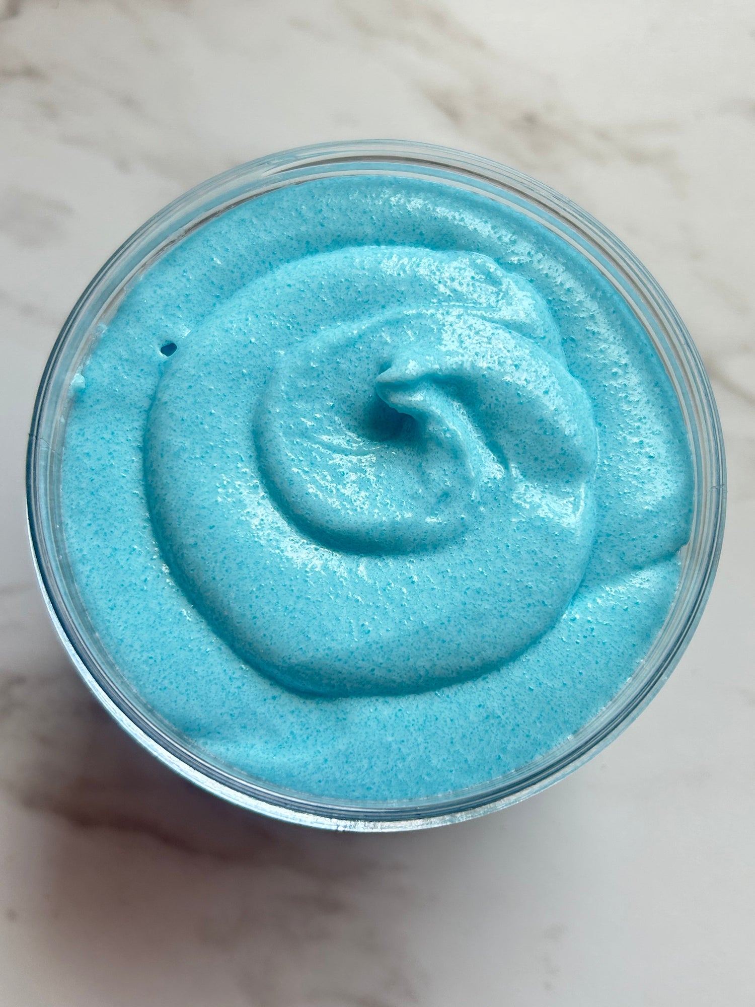 Open jar of sea-blue whipped sugar scrub with swirl surface