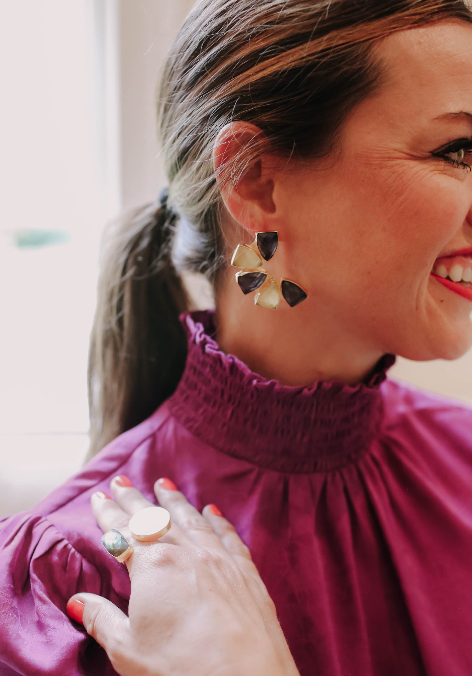 Purple and yellow flower stud earrings on a woman in a high-neck purple blouse