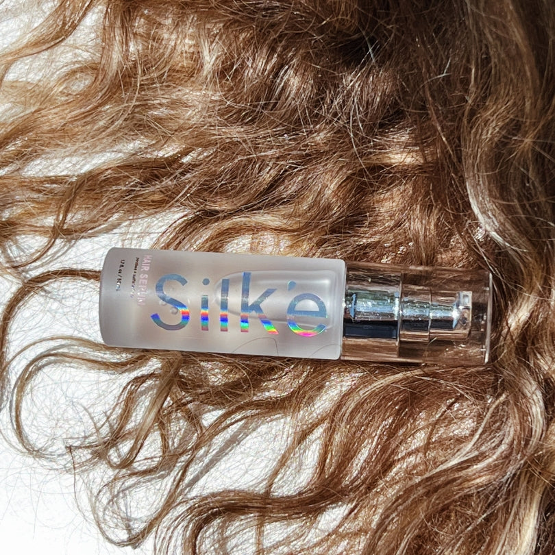 Hair repair serum bottle applicator held against wavy brown hair strands.