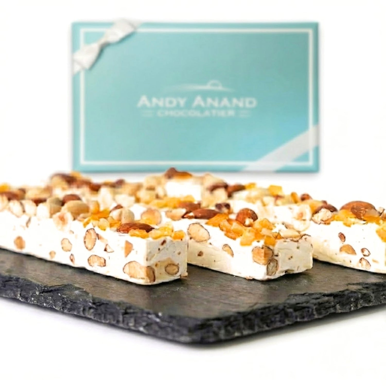 Orange peel nougat brittle bars with almond pieces on a dark slate board.