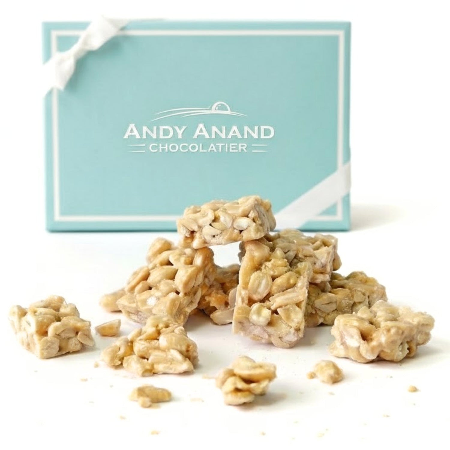 Peanut brittle pieces in a teal gift box, topped with chopped nuts