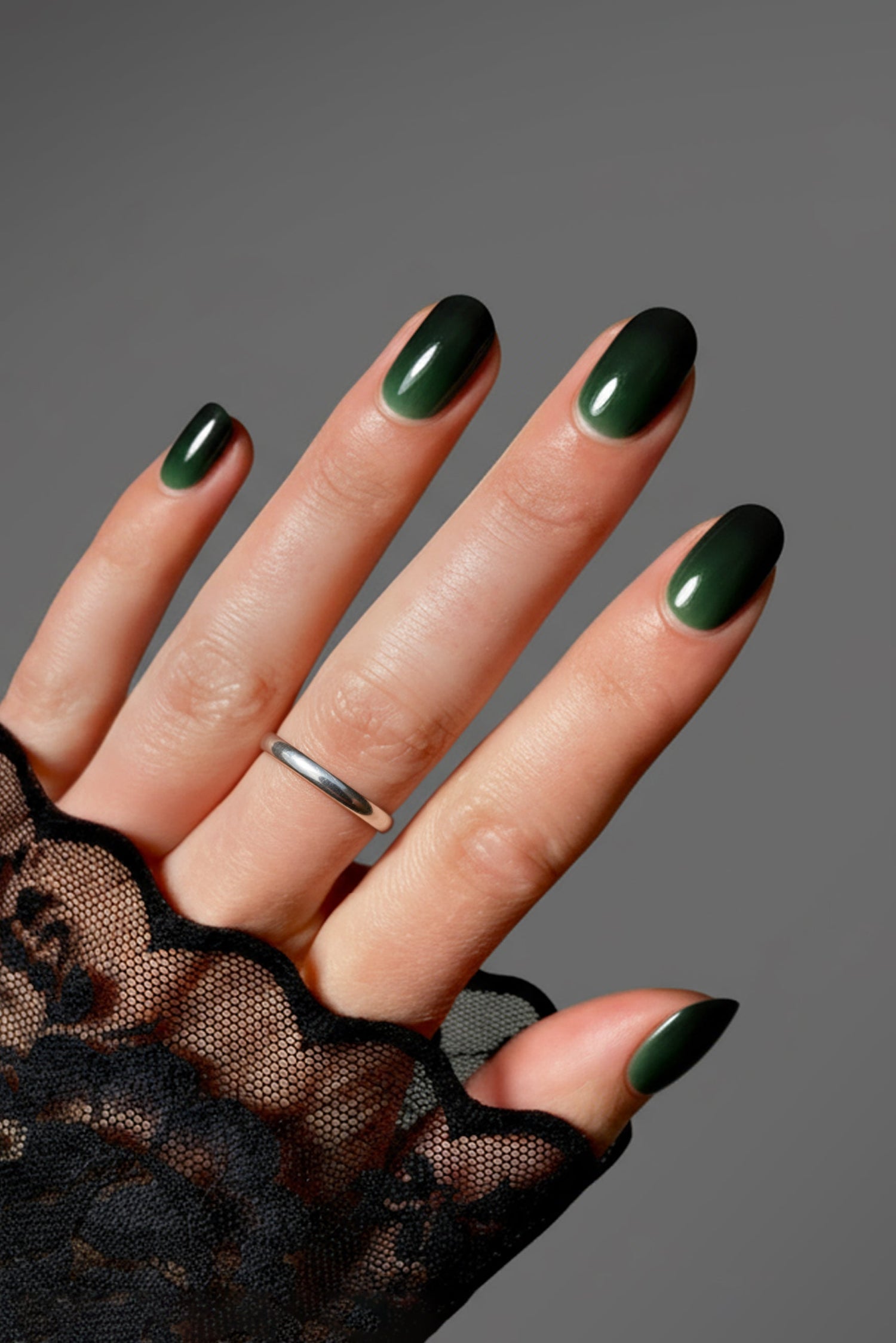 Hand wearing dark green glossy oval press-on nails with silver ring