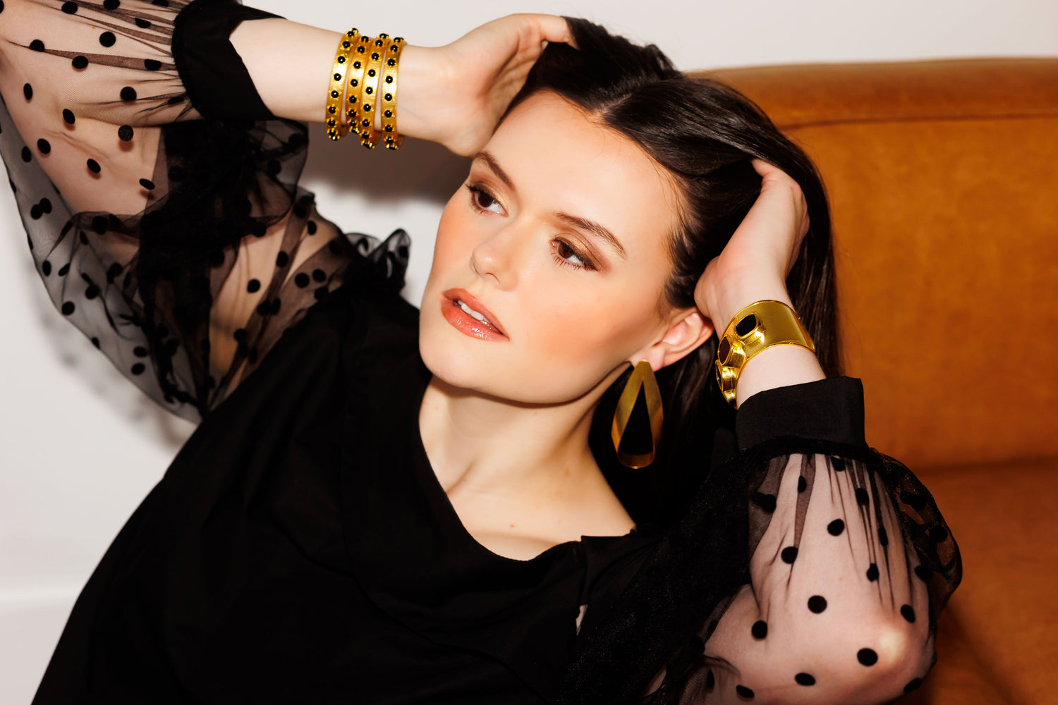 Gold teardrop hoop earrings with geometric cutouts, worn with a black and tan dress