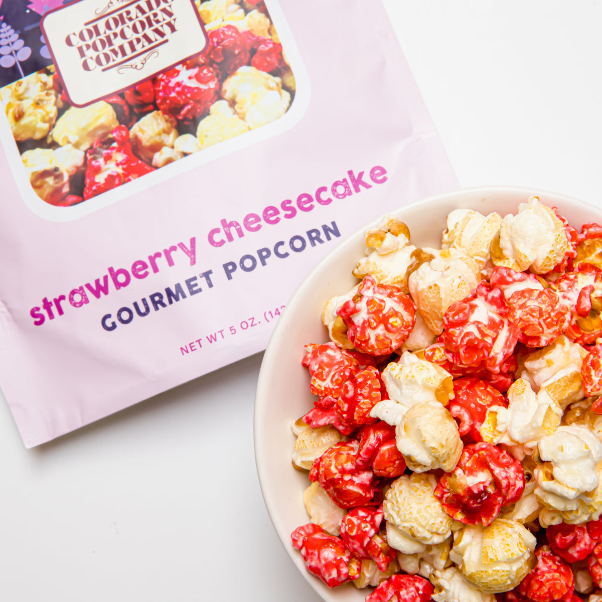 Strawberry cheesecake gourmet popcorn bag with bowl of red and white kernels