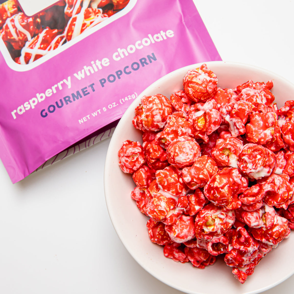 Raspberry white chocolate popcorn in a bowl with a purple bag partially visible