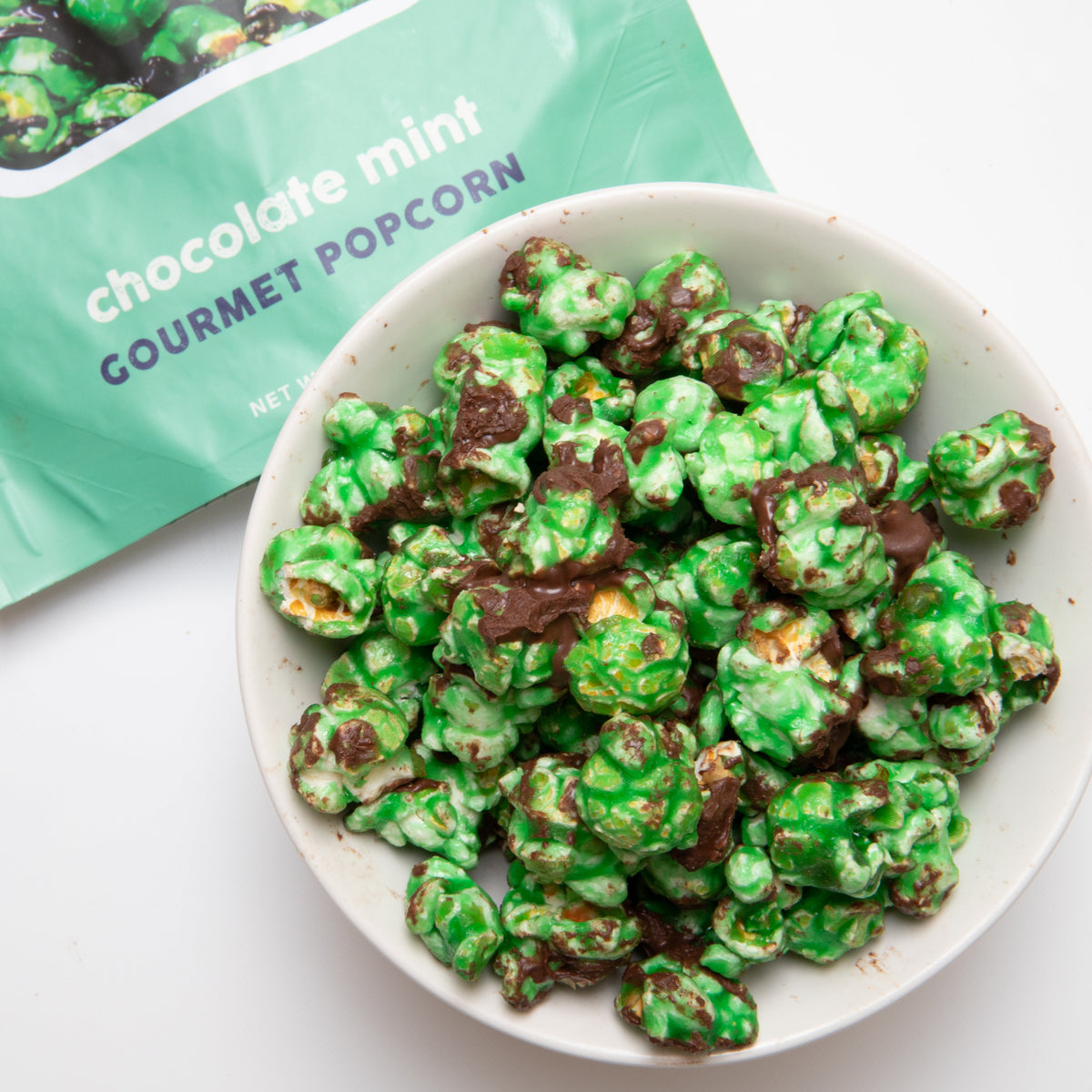 Chocolate mint popcorn in a white bowl, green coated kernels with chocolate bits