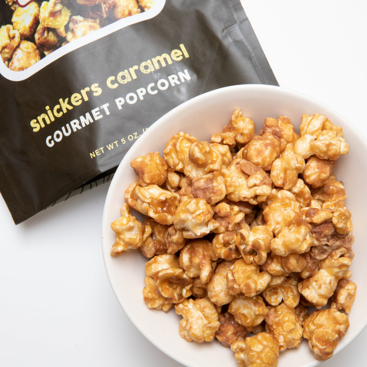 Snickers caramel gourmet popcorn in a white bowl with snack pouch nearby
