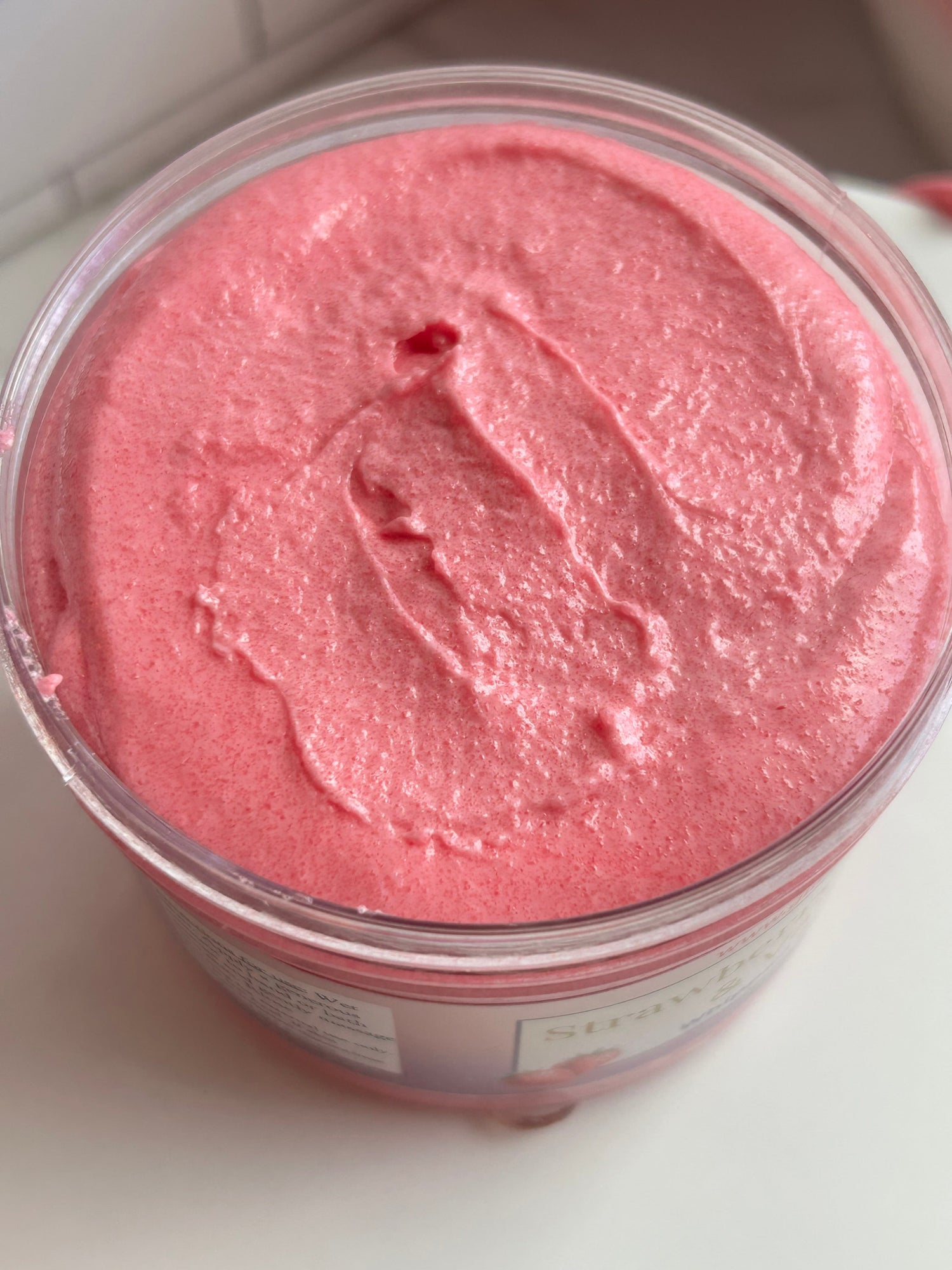Pink whipped body scrub texture in open clear jar, glossy swirl surface