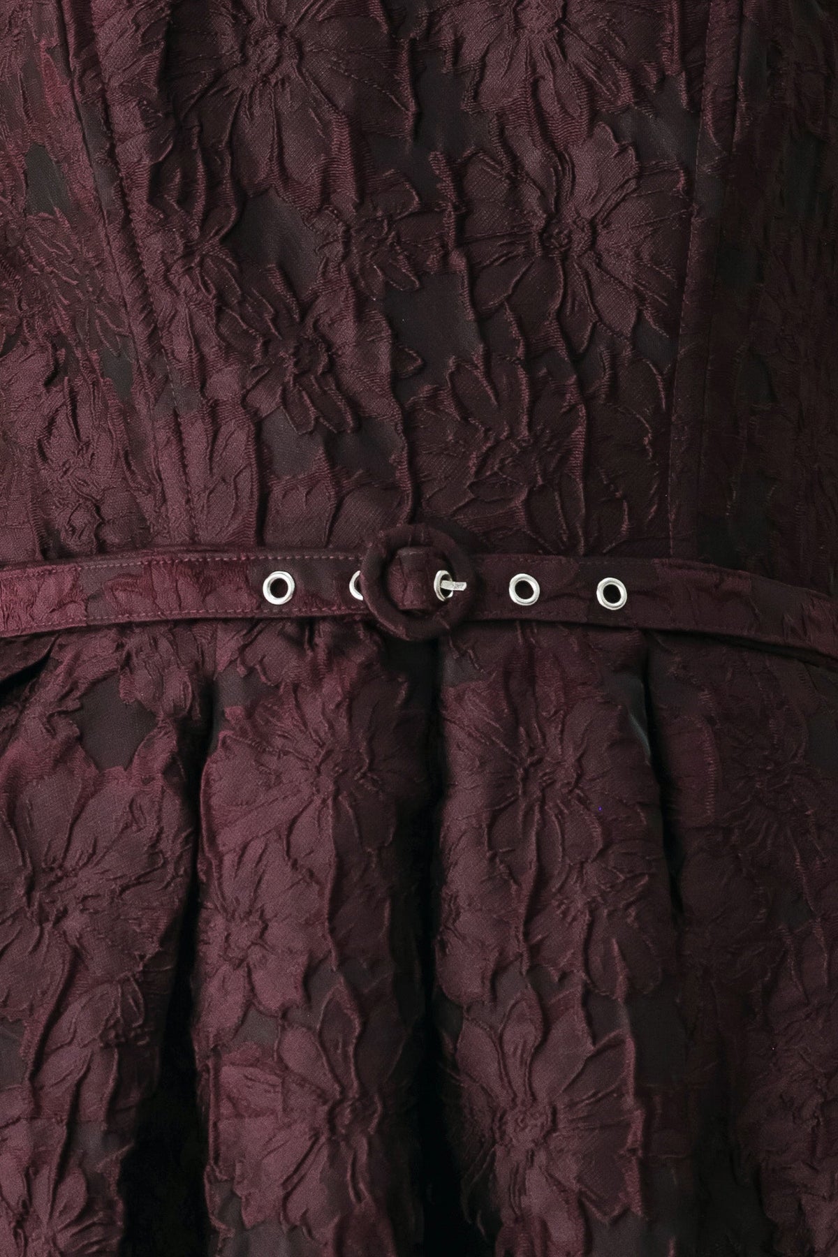 Close-up of burgundy woven fabric with grommet belt and circular button hardware