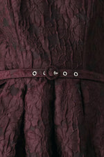 Close-up of burgundy woven fabric with grommet belt and circular button hardware