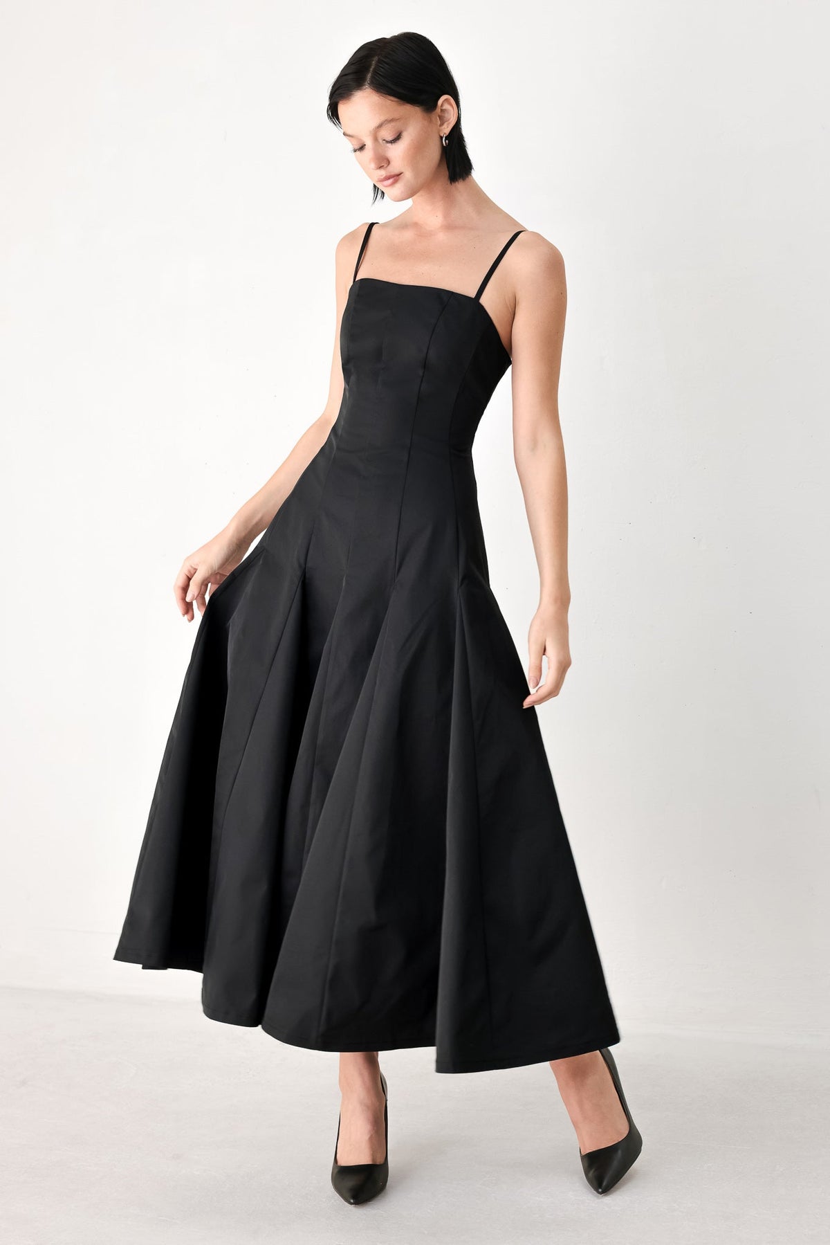 Black midi dress with thin straps and flared A-line skirt with pleated volume