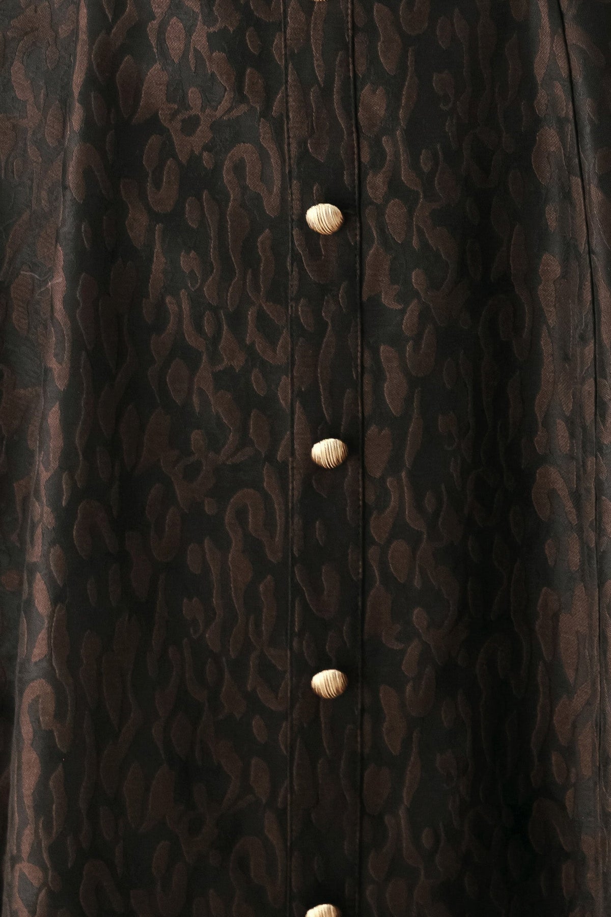 Close-up of dark patterned fabric with gold button placket down the center