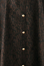 Close-up of dark patterned fabric with gold button placket down the center