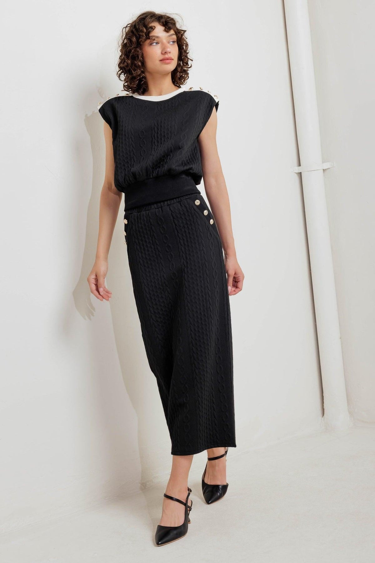 Black knit midi skirt with fitted waist, gold button accents, and front slit