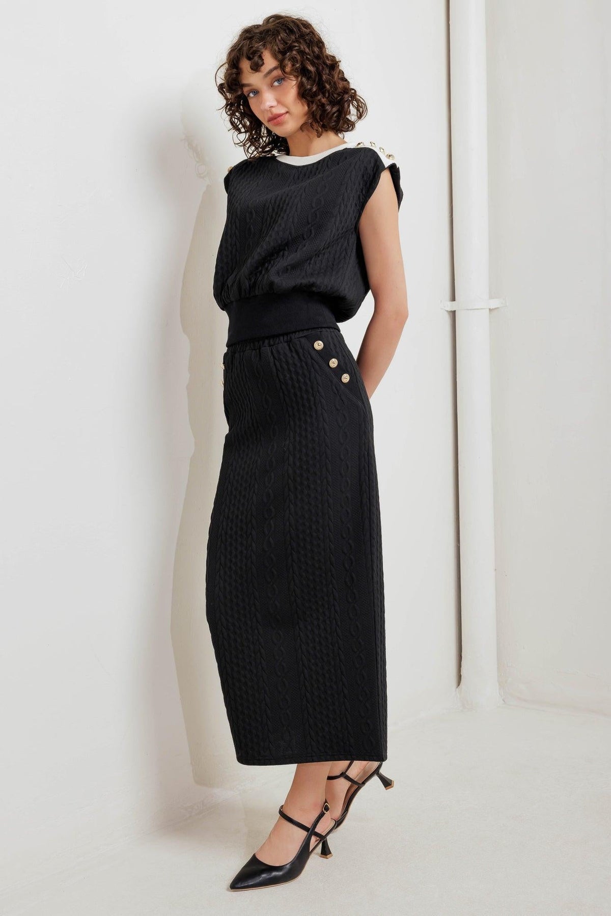 Black knit midi skirt with textured fabric, fitted waist, and gold button accents