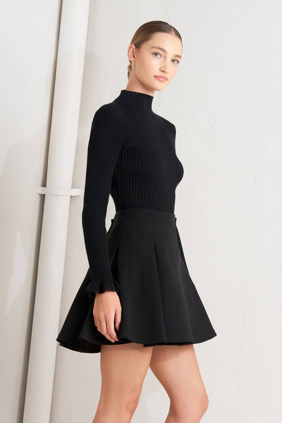 Black high-waist mini skirt with knife pleats and flared hem, angled view