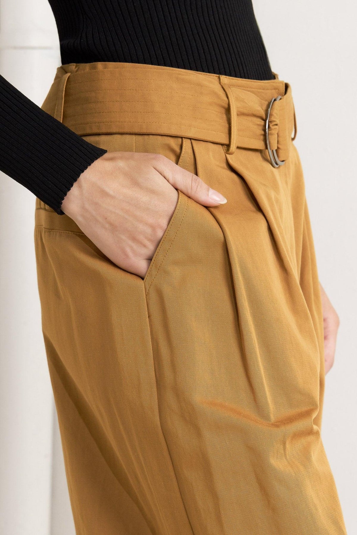 Camel woven pants close-up: belt buckle, stitched seams, and deep front pockets