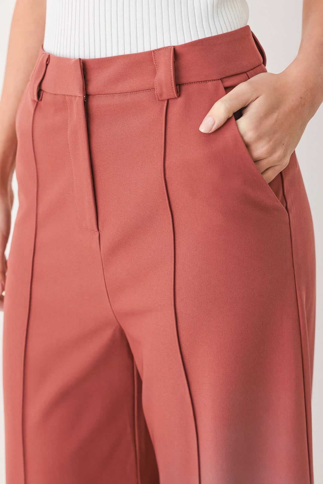 Dried rose woven pants close-up: high-waist belt loops, pleated front, center seam.