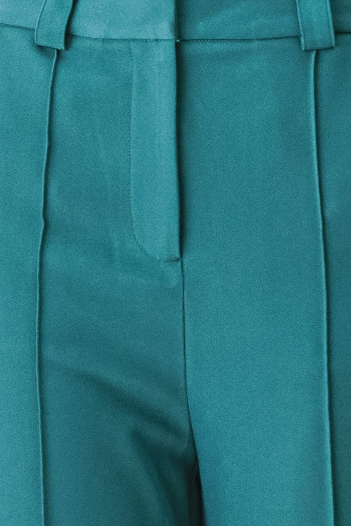 Teal woven pants close-up: central front seam and pleated front with smooth panels.
