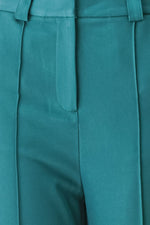 Teal woven pants close-up: central front seam and pleated front with smooth panels.
