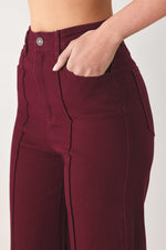 Close-up of women’s burgundy twill pants: button waistband, belt loops, and pocket opening.