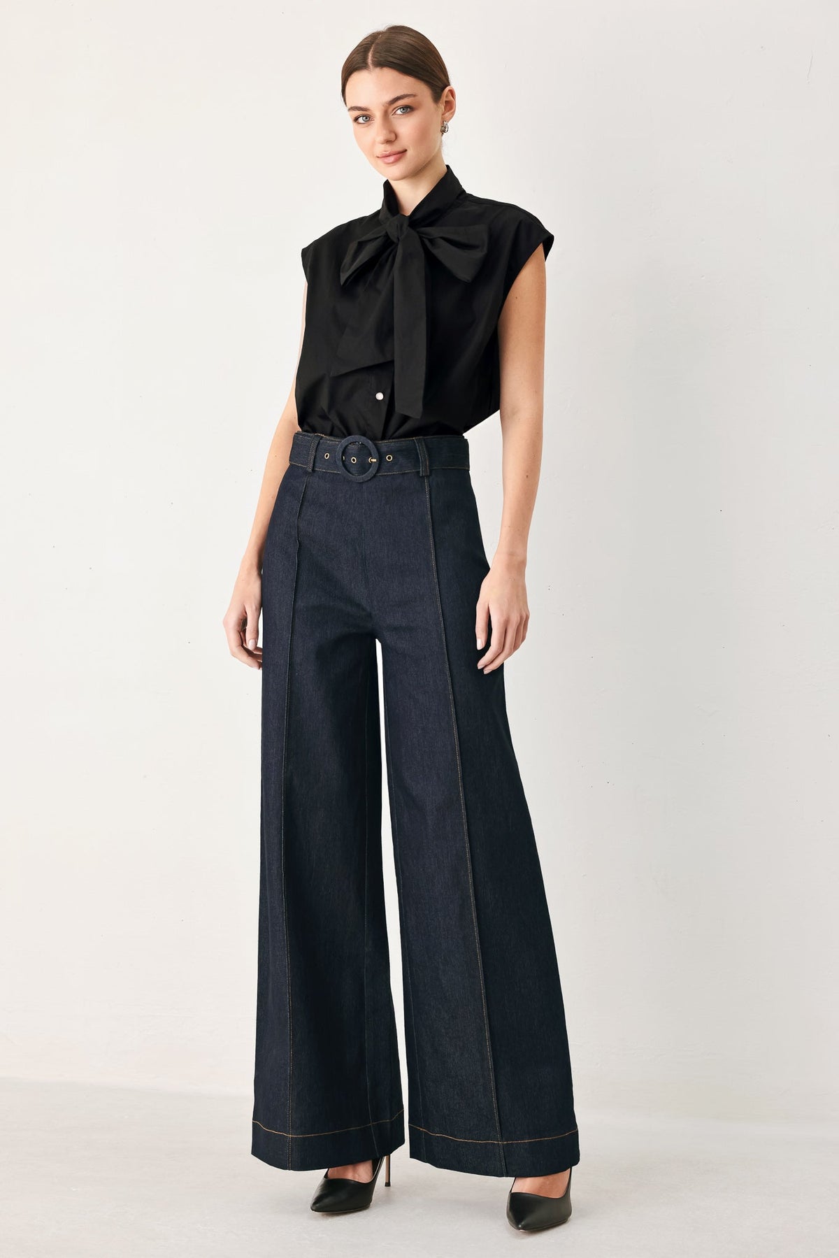 Dark denim wide-leg pants with buckle belt, center creases, and contrast stitching