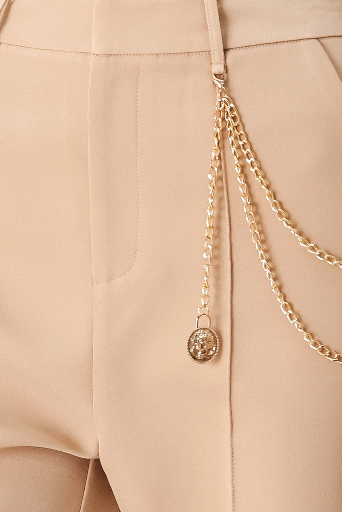 Camel woven pants close-up: gold-tone drape chain and round charm at pocket