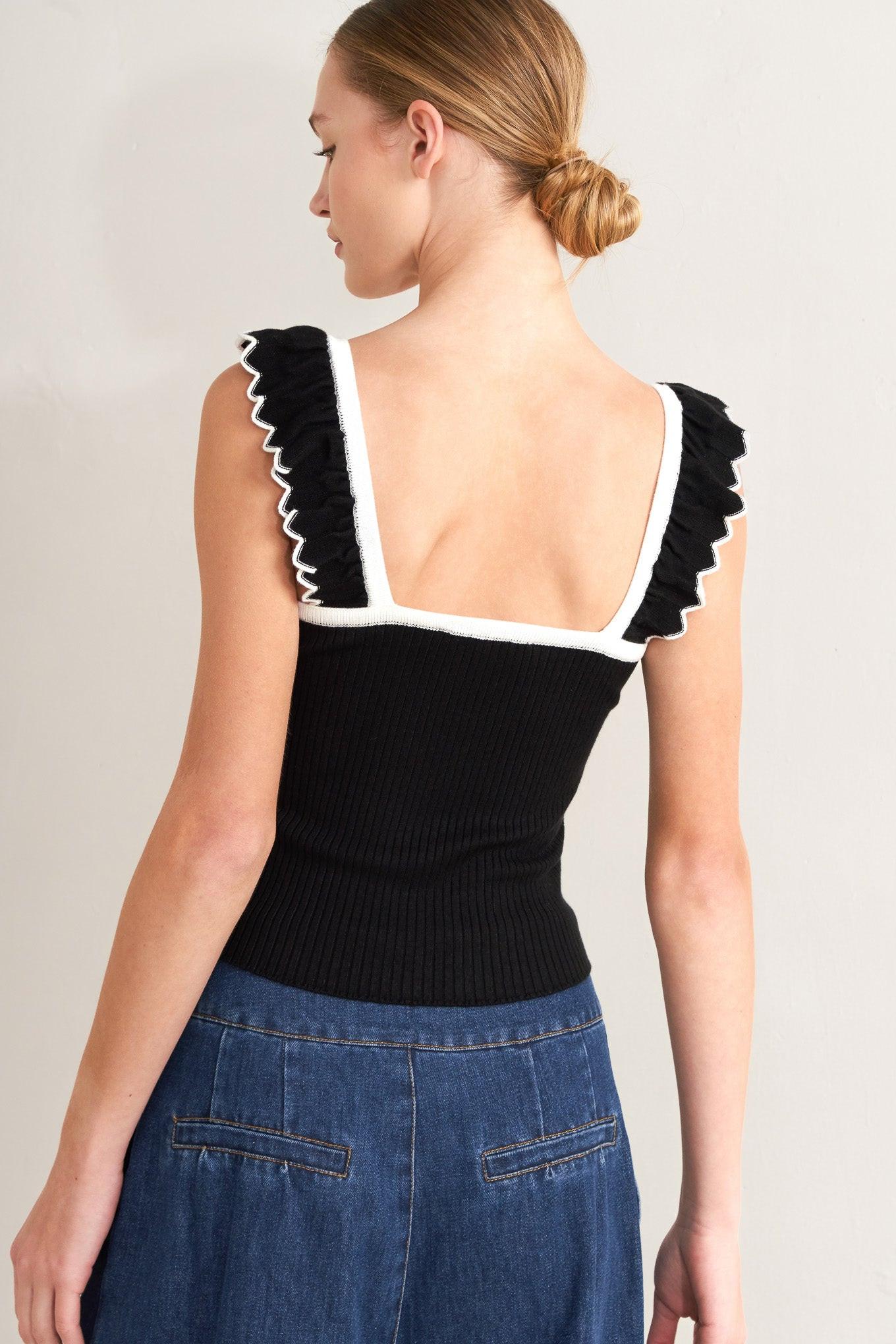 Black knit sweater top viewed from back with white trim on square back and shoulder ruffles