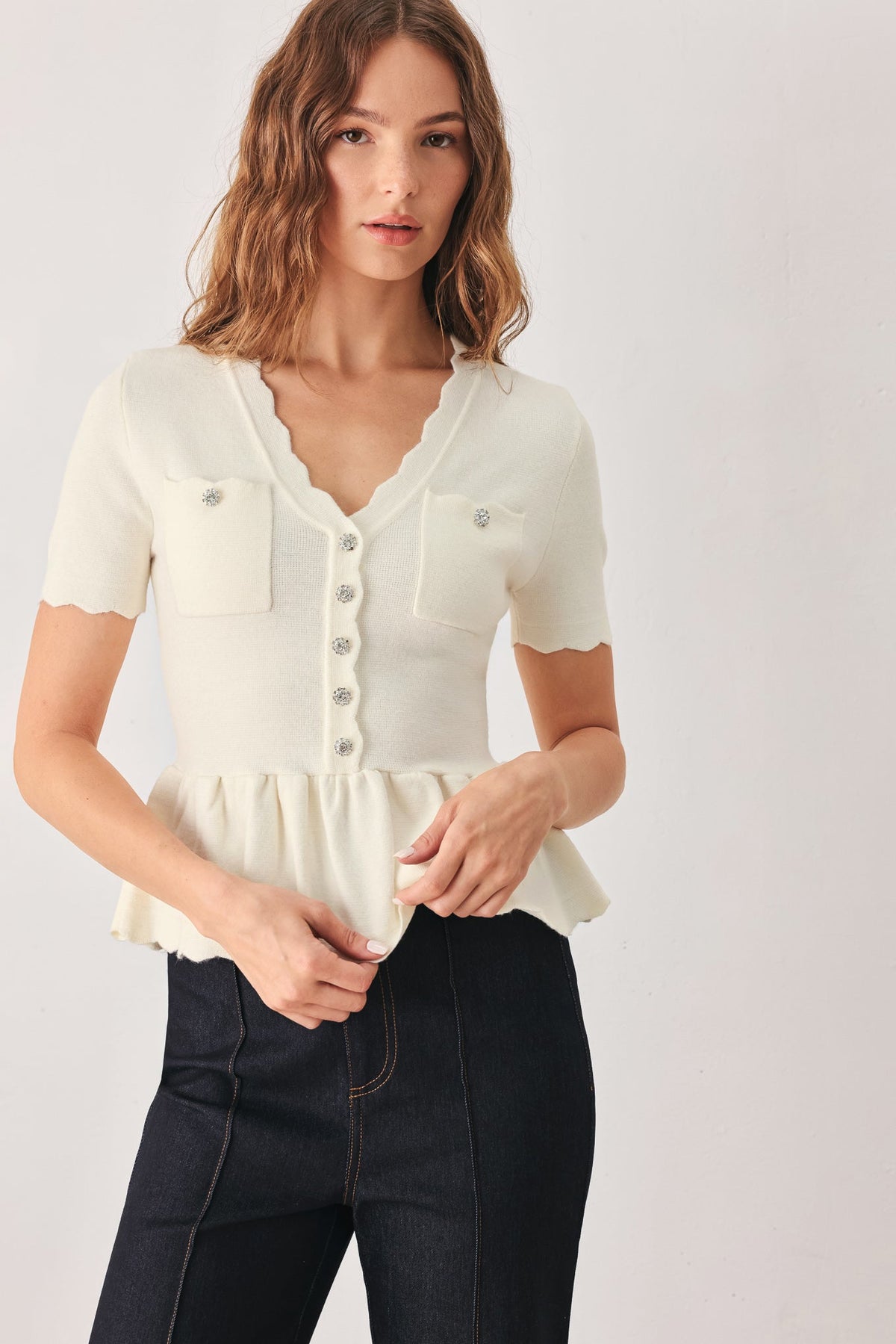 Off-white sweater top with scalloped V-neck, button placket, chest pockets, peplum