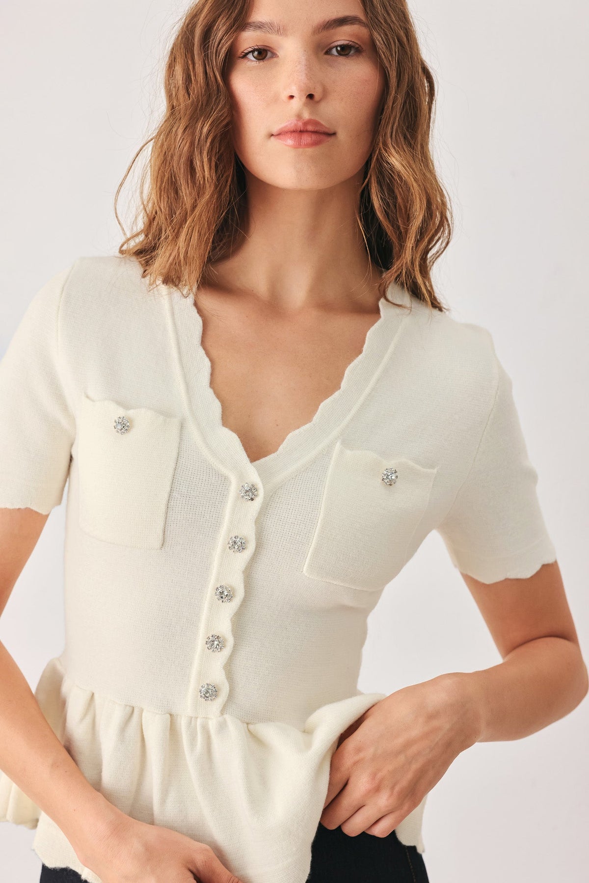 Cream knit sweater top with scalloped V-neck and front button closure; chest pockets