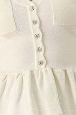 Close-up off-white knit sweater top: button front with jewel accents and peplum ruffle