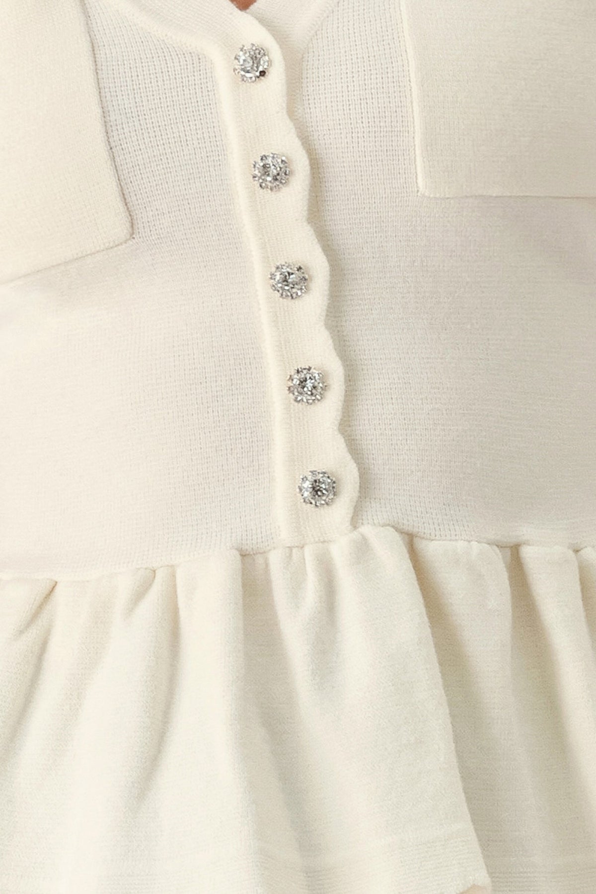 Close-up off-white knit sweater top: button front with jewel accents and peplum ruffle