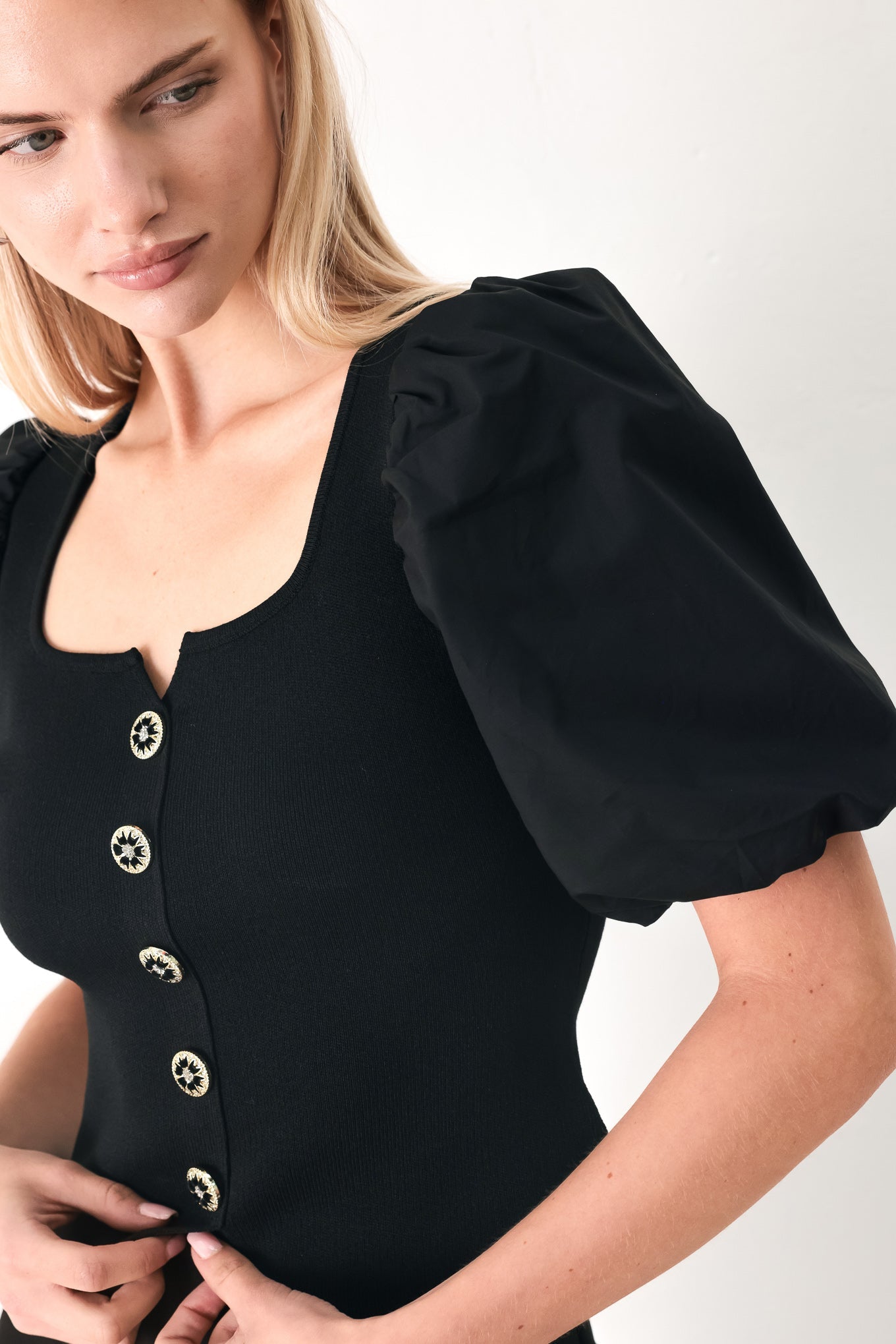Black sweater-knit top with short puff sleeves, round neckline, and gold button front