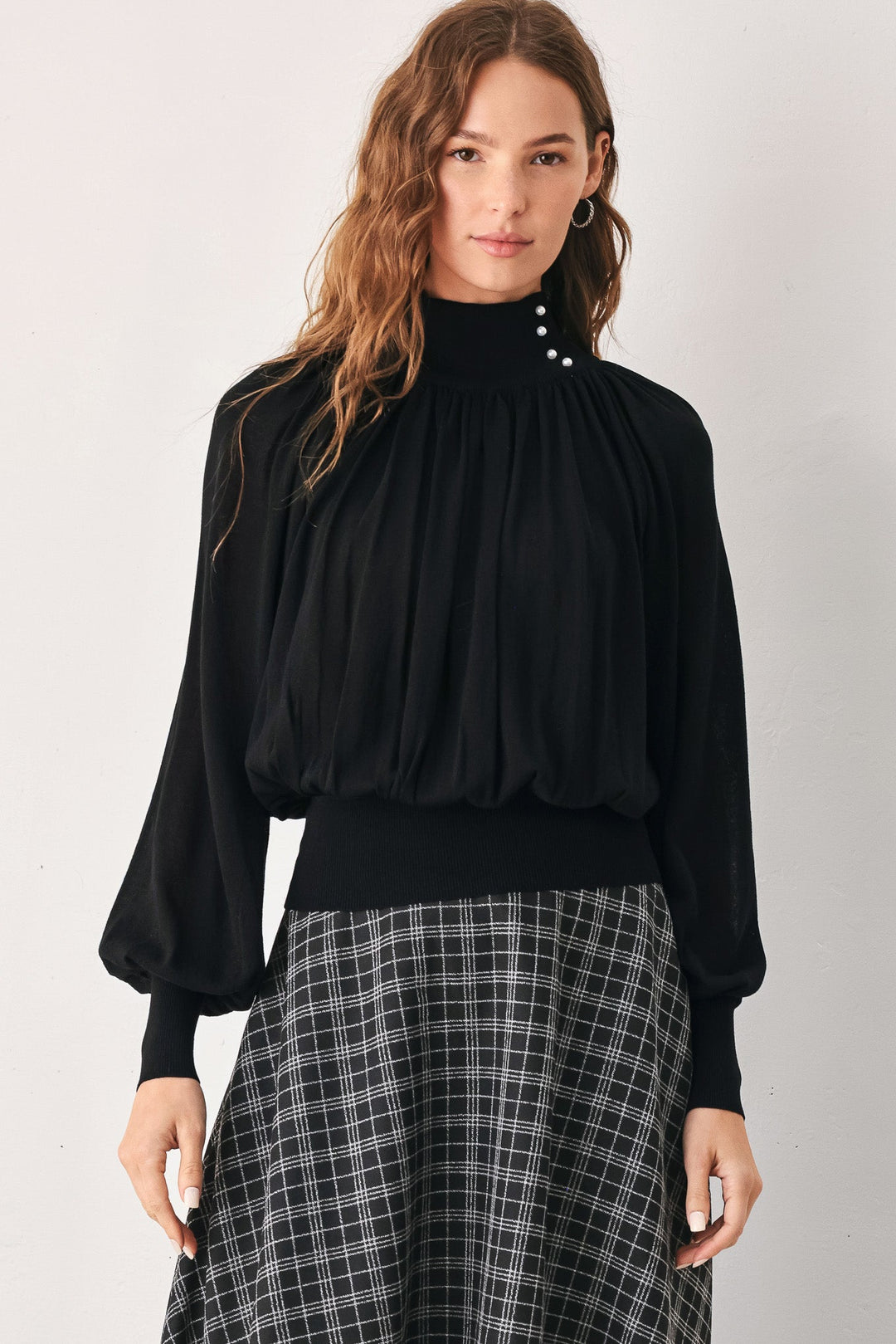 Black high-neck draped knit top with buttoned collar and voluminous long sleeves