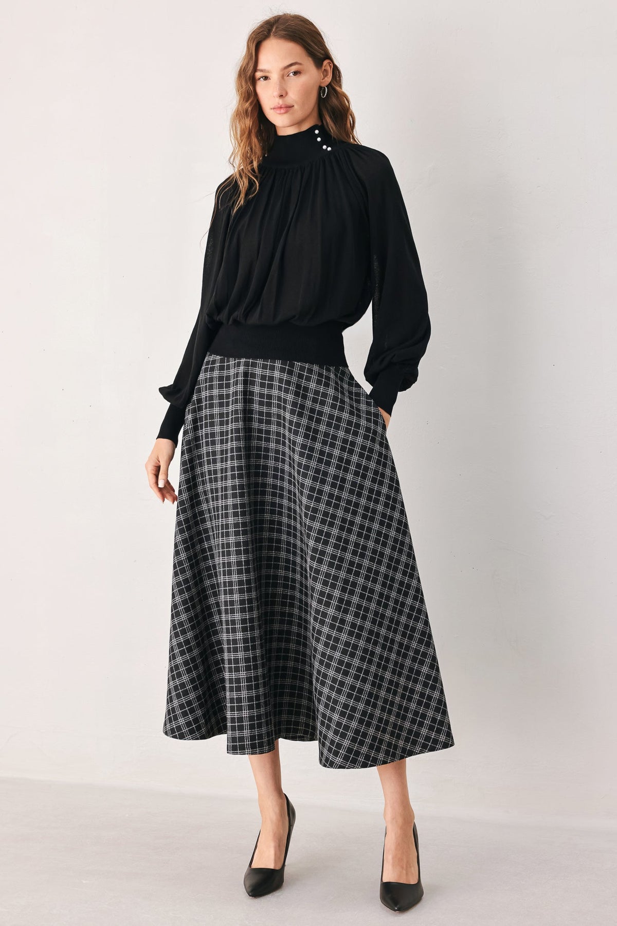 Black high-neck draped knit top with buttoned collar and gathered, flowing silhouette