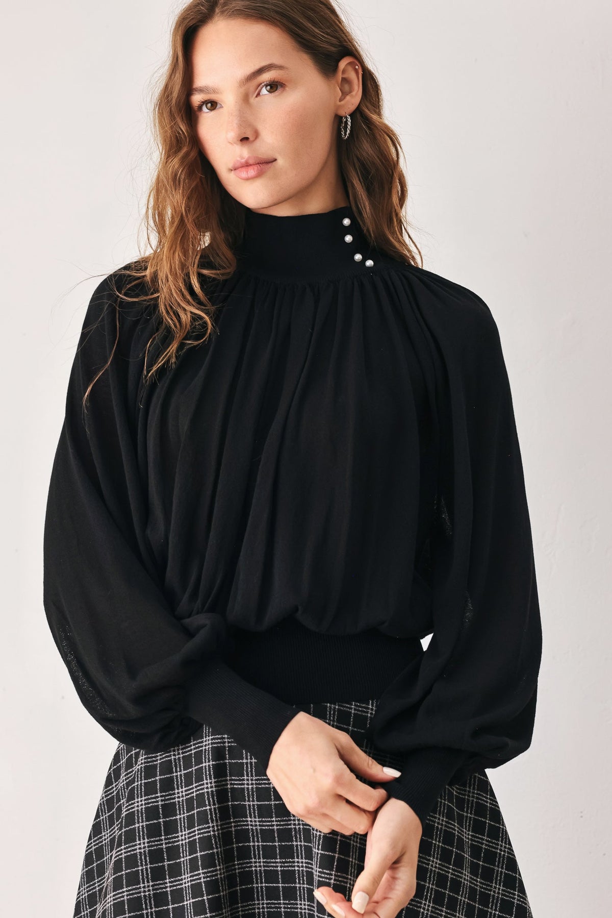 Front view: black draped knit top with high collar and small button detail at neckline