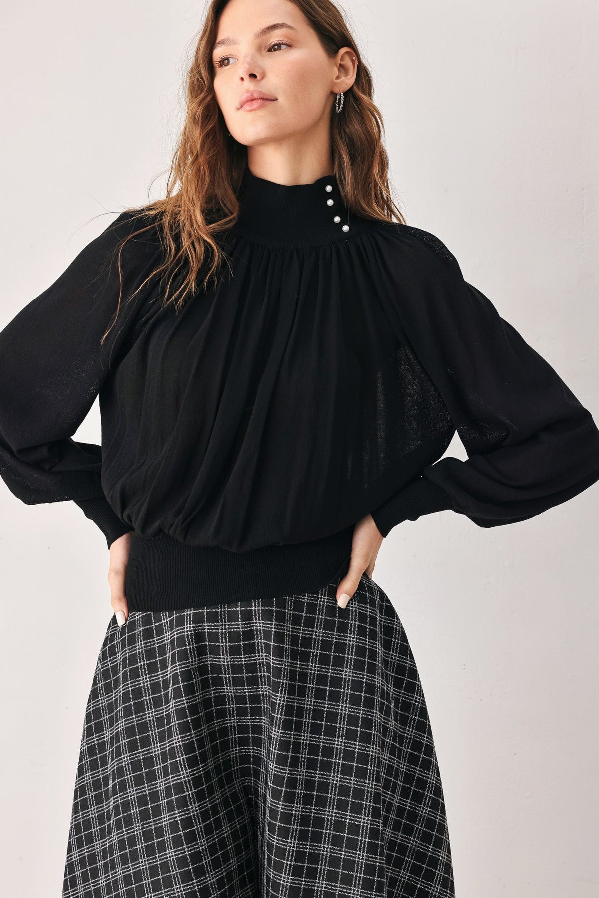 Black draped knit top with gathered yoke, buttoned high neck, and wide long sleeves