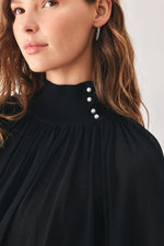 Close-up: black knit top with high collar and small round buttons along neckline
