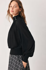 Black draped knit top with long balloon sleeves and buttoned high neckline