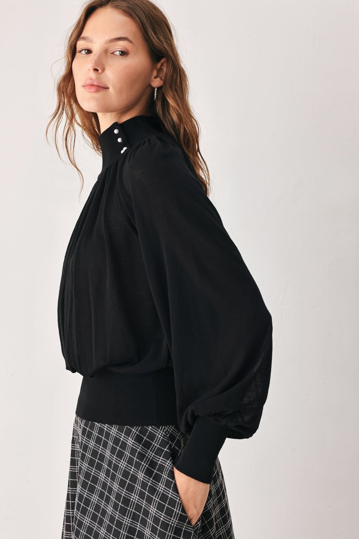 Black draped knit top with long balloon sleeves and buttoned high neckline
