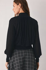 Back view: black draped knit top with gathered yoke and voluminous sleeves