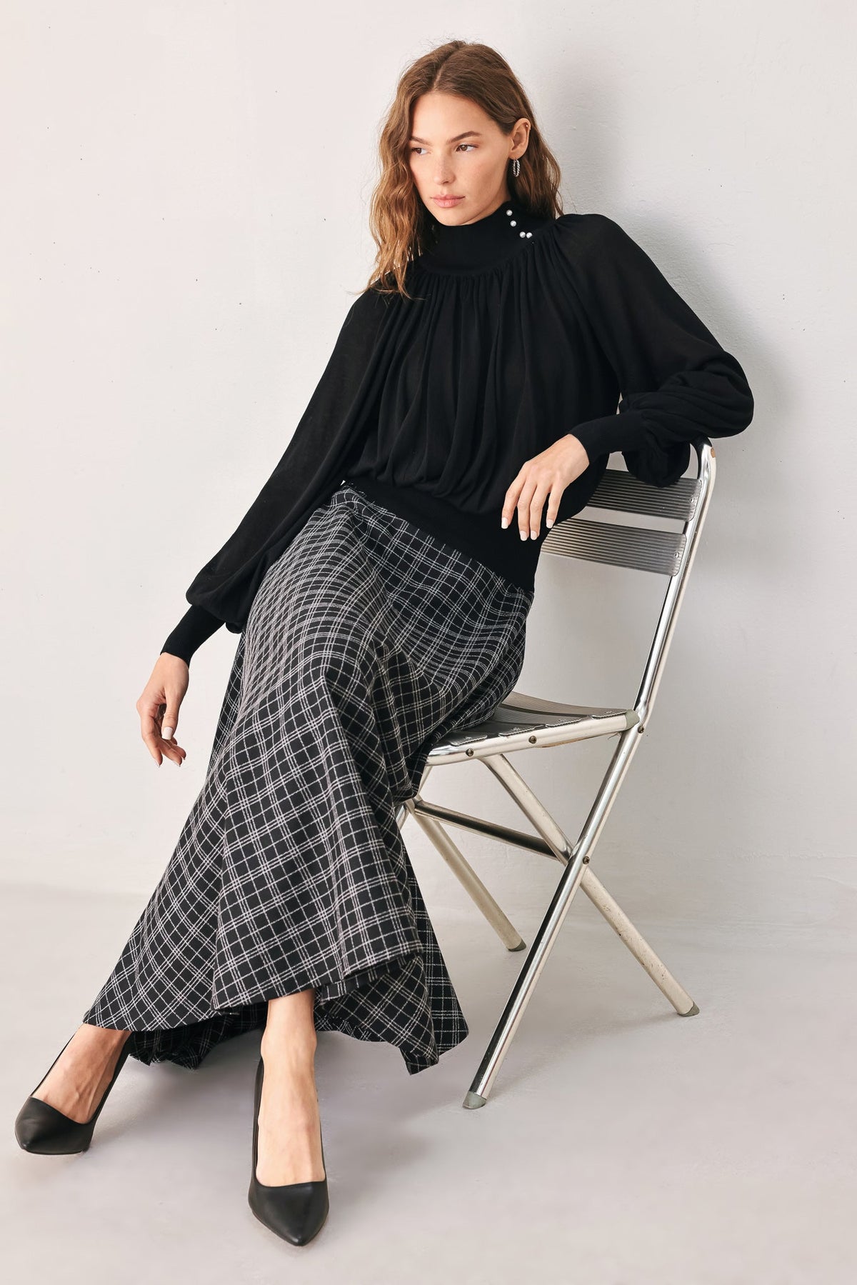 Black draped knit top with high neck, buttoned collar, and oversized balloon sleeves