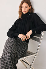 Black draped knit top with high neck and buttoned collar, gathered waist, long sleeves