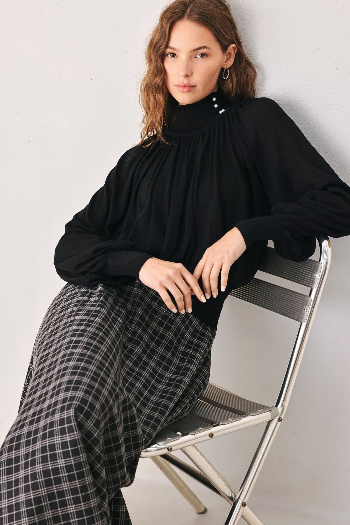 Black draped knit top with high neck and buttoned collar, gathered waist, long sleeves