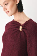 Close-up of burgundy sweater neckline with cinched collar and gold charm detail