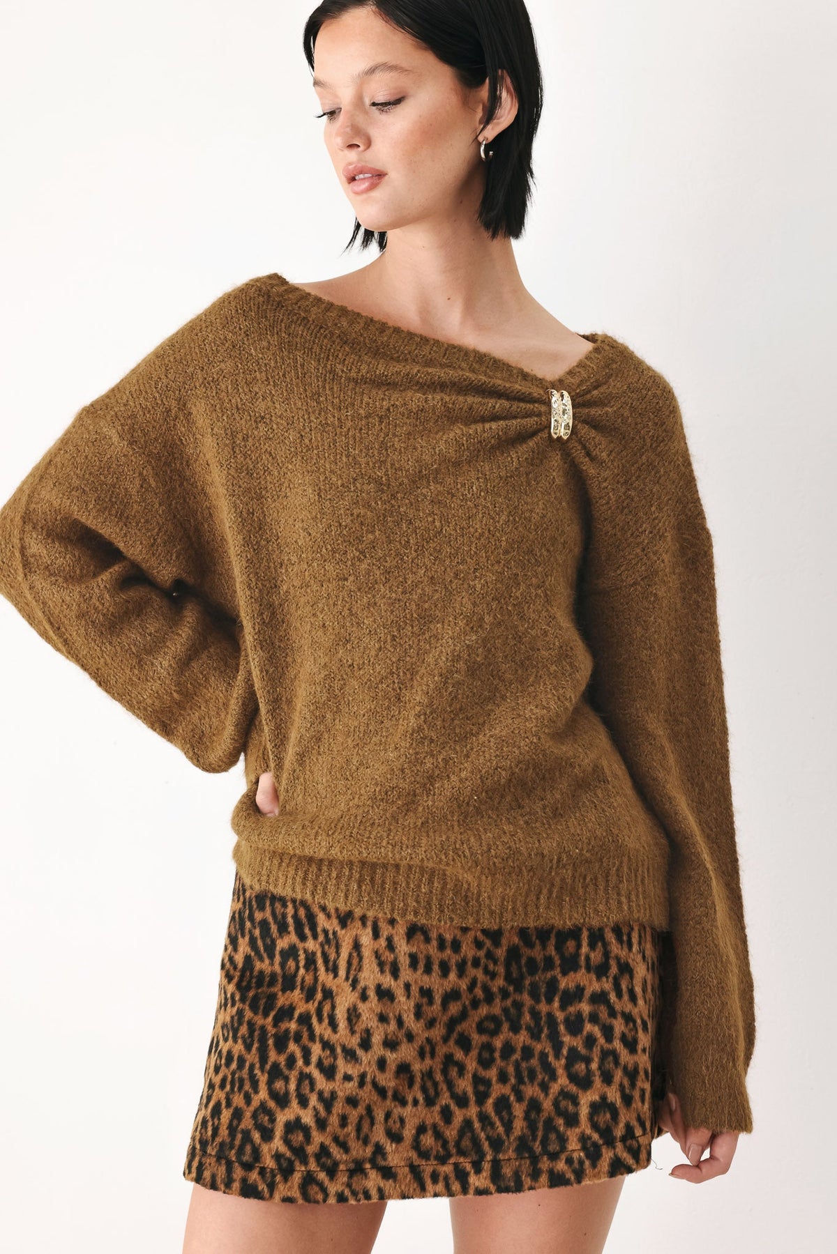 Camel-brown knit sweater with one-shoulder cinched neckline and decorative clasp