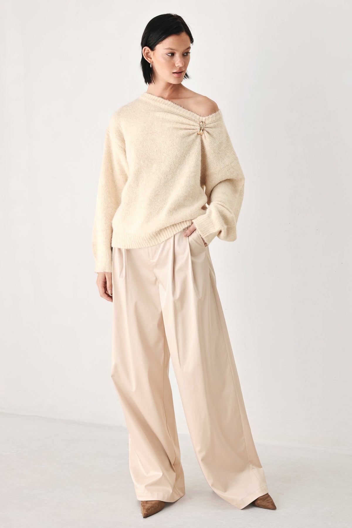 Ivory knit sweater with one-shoulder cinched neckline and clasp detail
