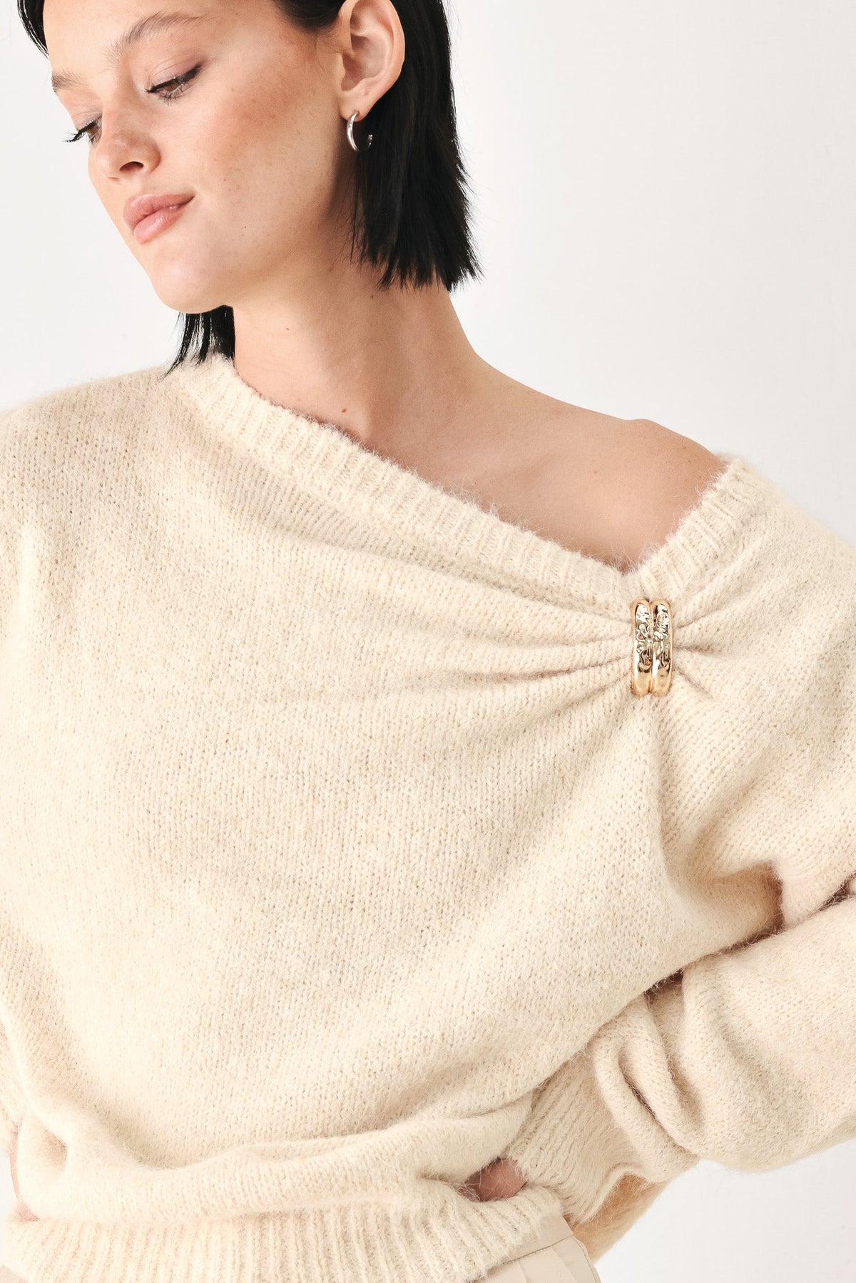 Ivory sweater with one-shoulder cinched neckline and small decorative clasp