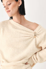Ivory sweater with one-shoulder cinched neckline and small decorative clasp